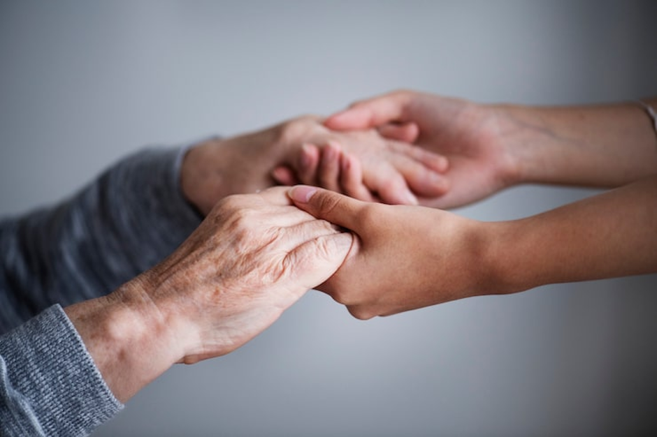 A younger pair of hands holding an older person's hands