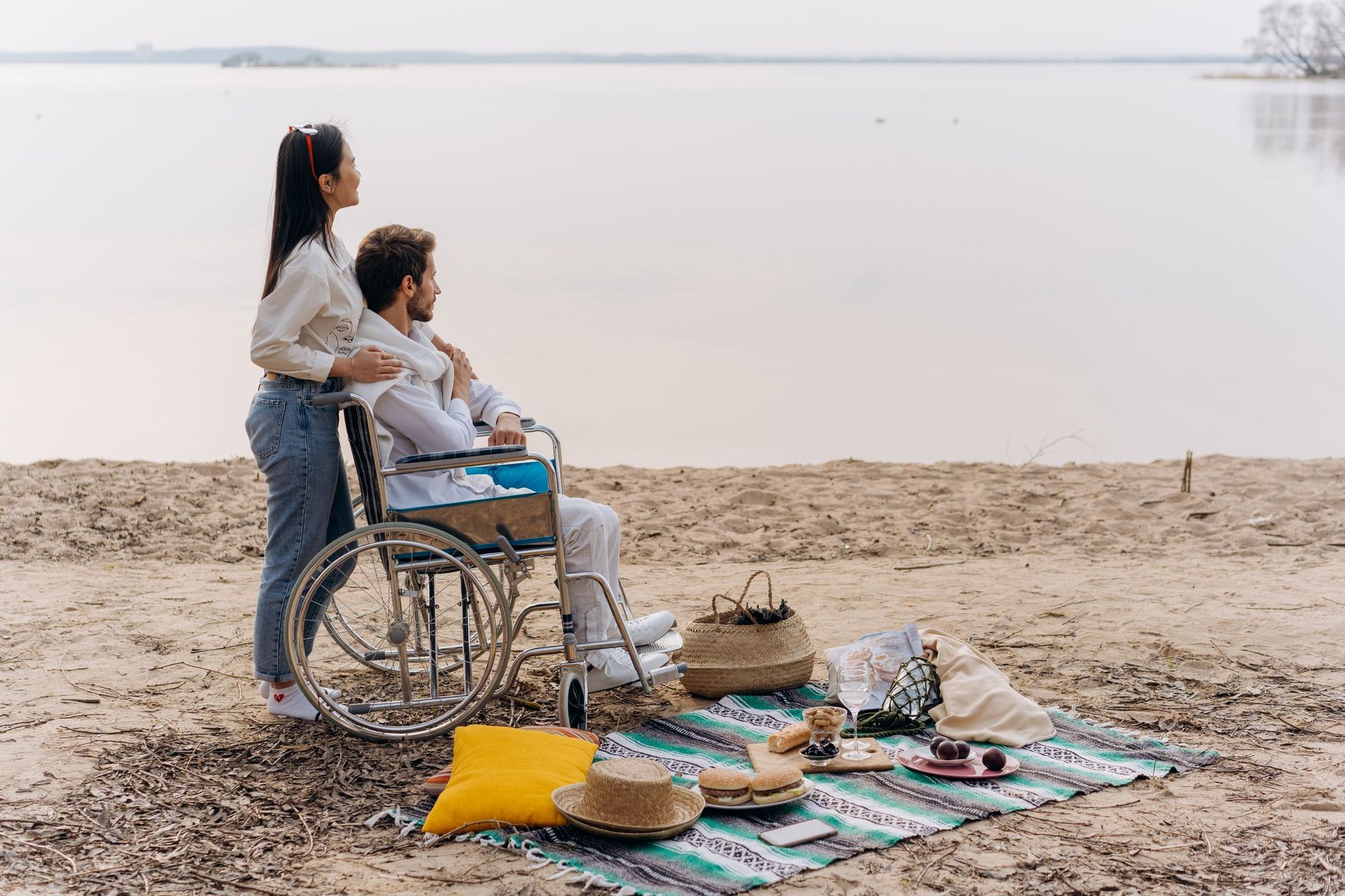 A man in a wheelchair and a woman having a picnic on the beach