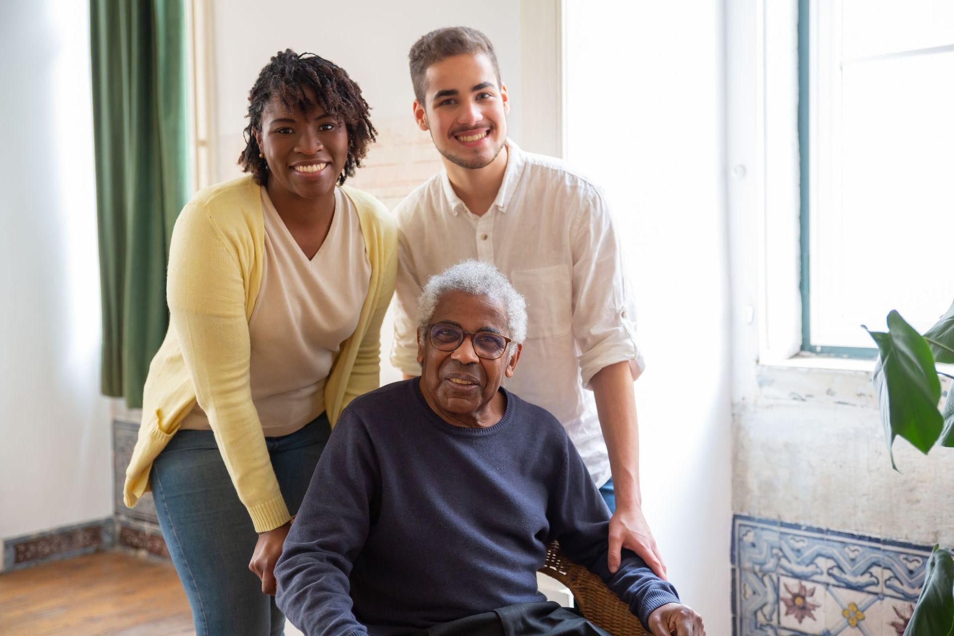 Two smiling carers standing behind an older man in his chair