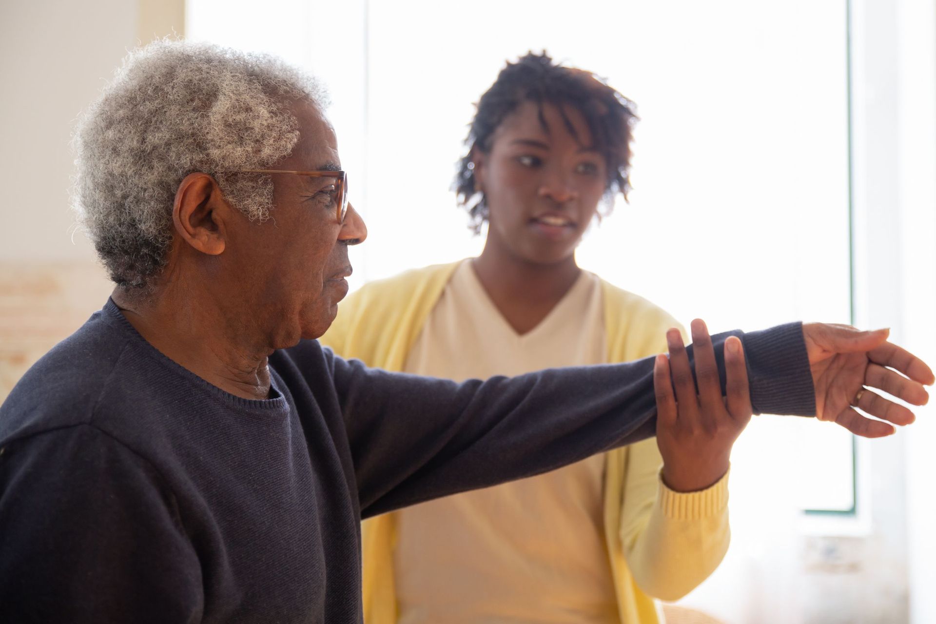 A carer supporting an older man's arm through a stretching exercise