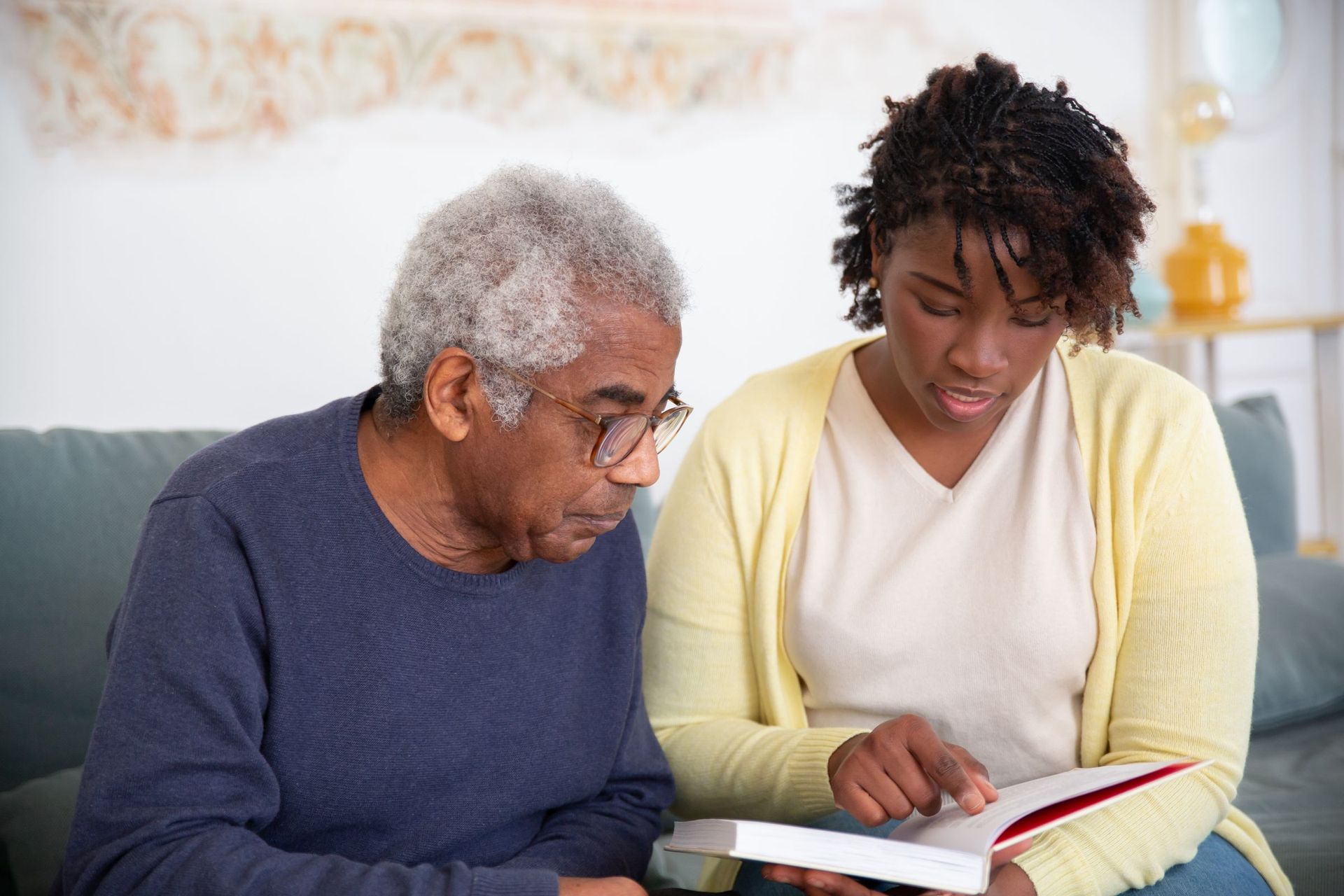 A carer and an older man looking through a book together on the sofa