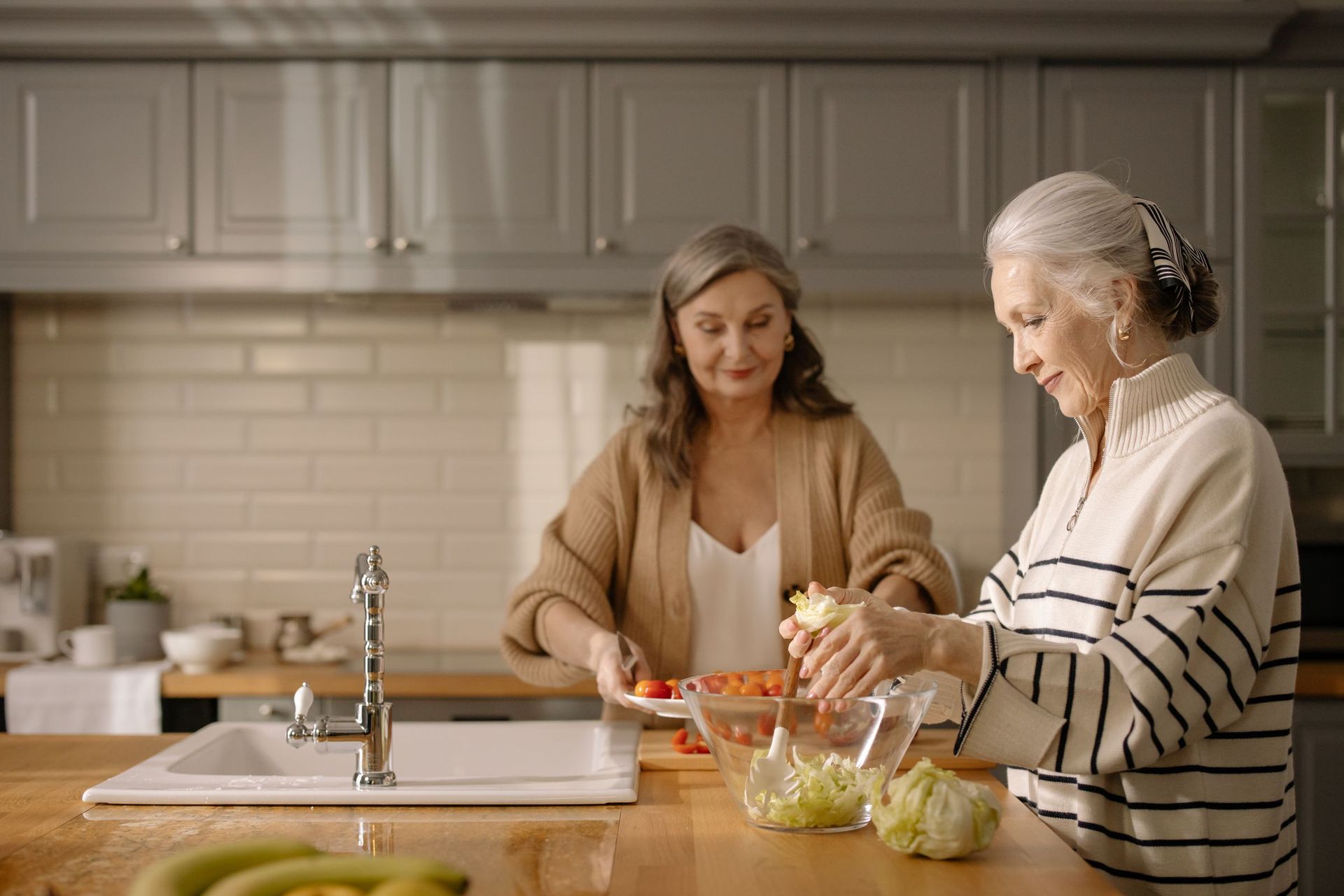 Two older women making a salad together in the kitchen
