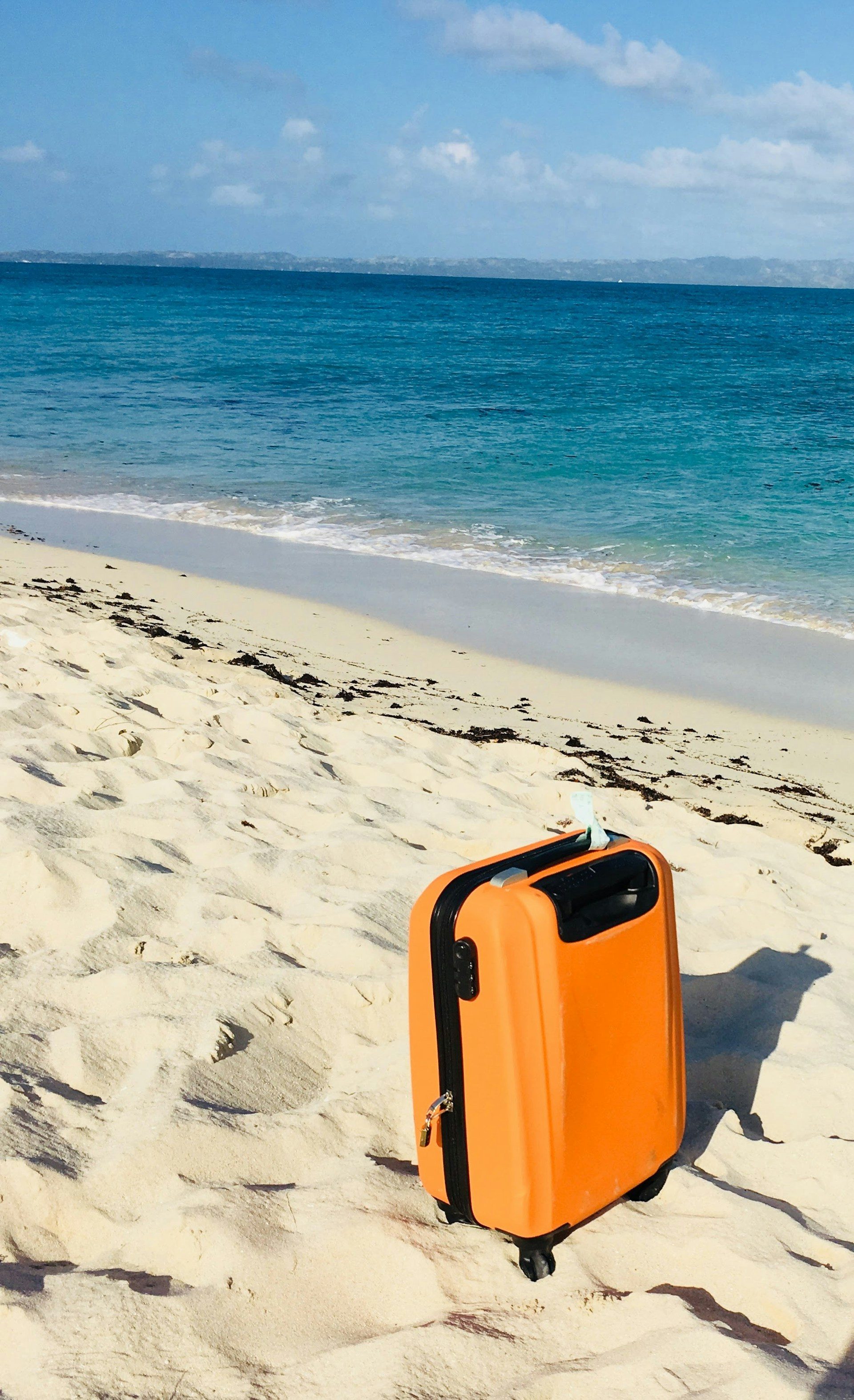 A suitcase standing on a white sand beach beside clear blue sea