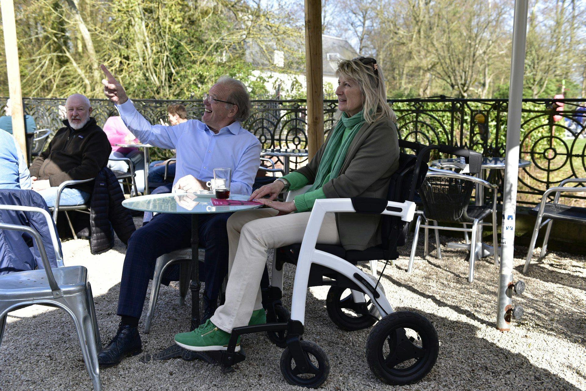 Two people chatting at an outdoor café table, one using a wheelchair