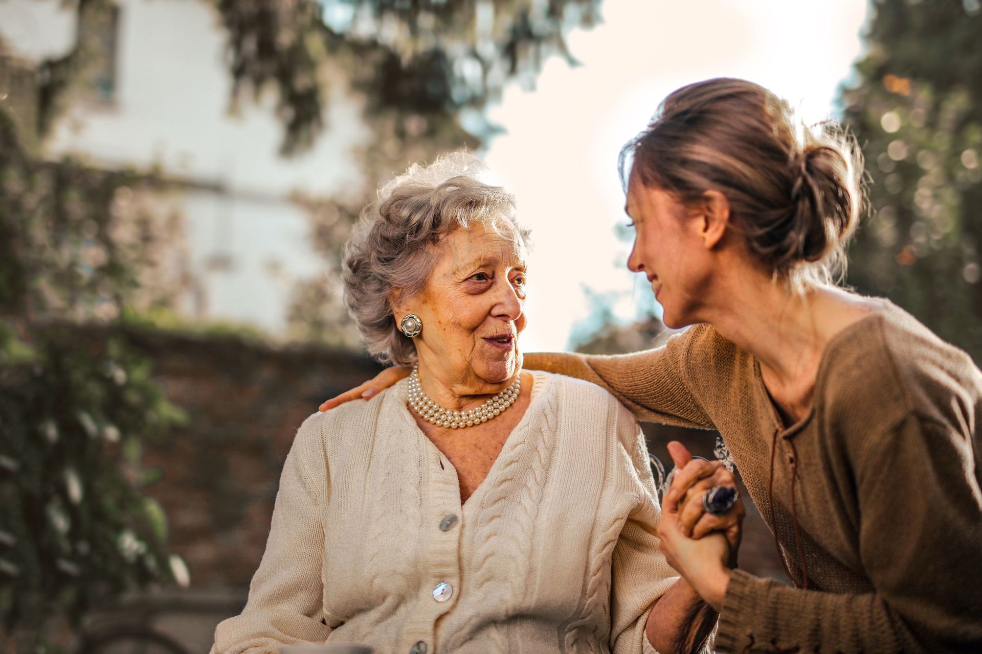 An older woman and a younger woman smiling and holding hands outdoors