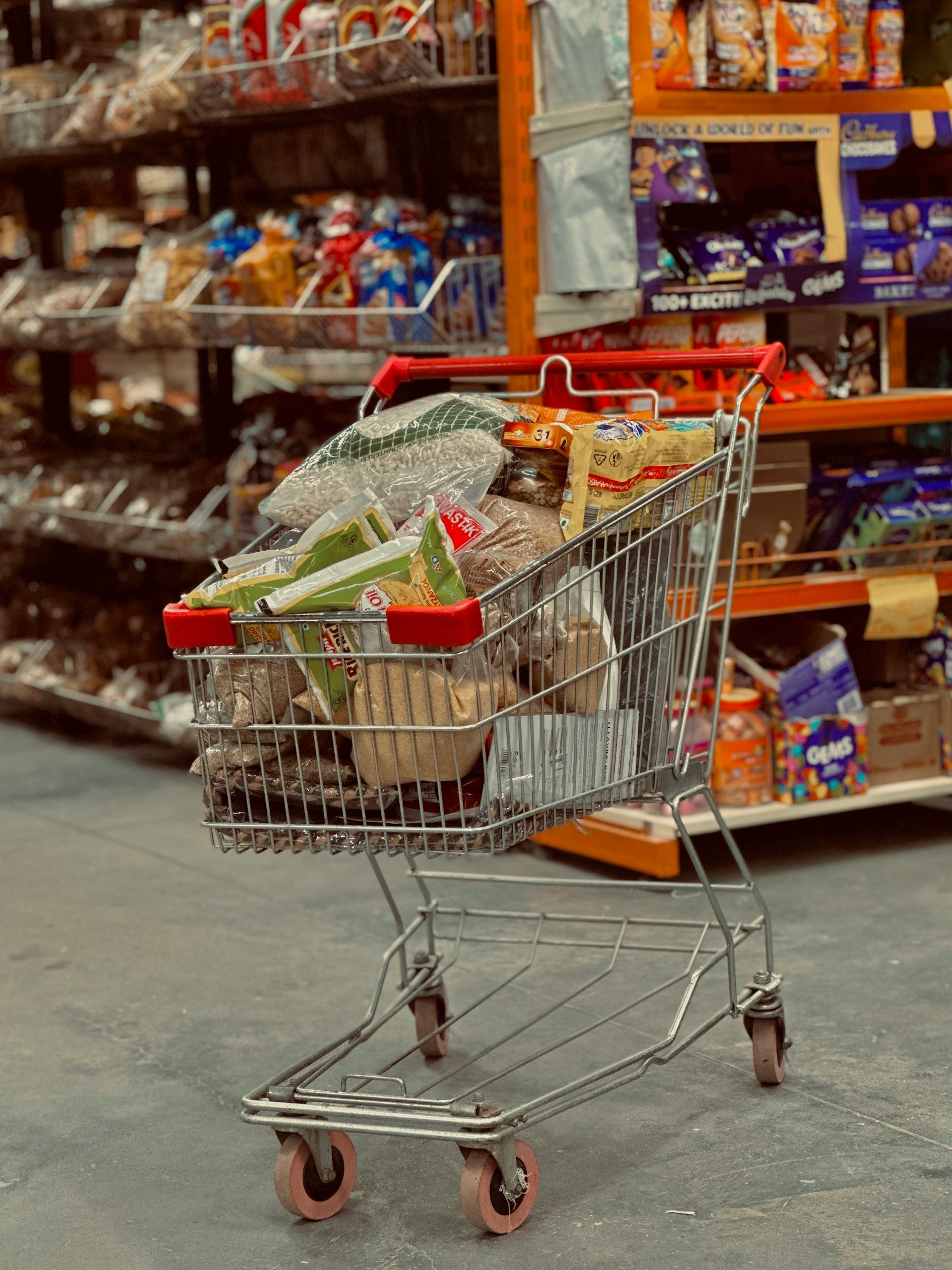 A full shopping trolley in a supermarket aisle
