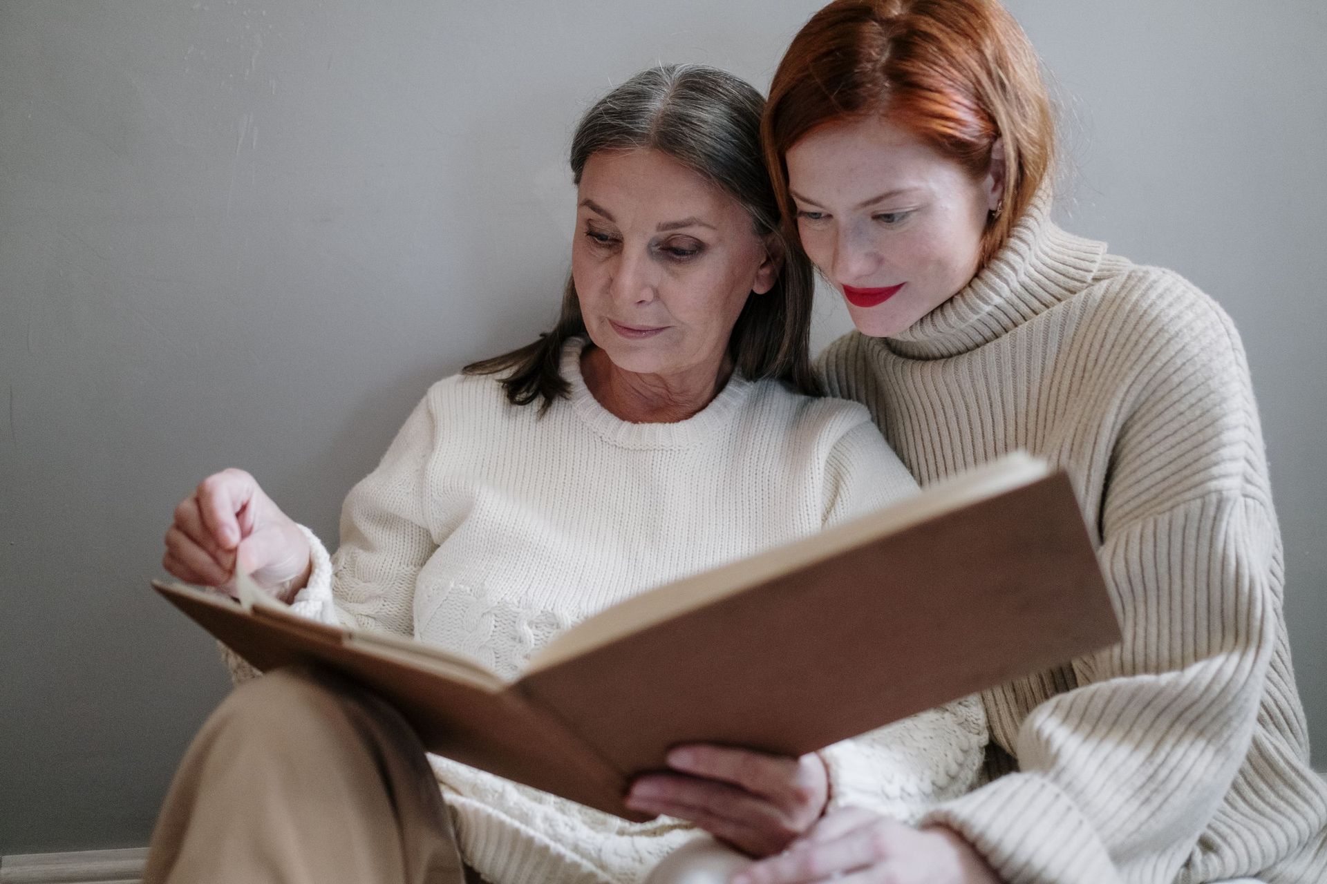 A younger woman and an older woman reading a book together on the sofa