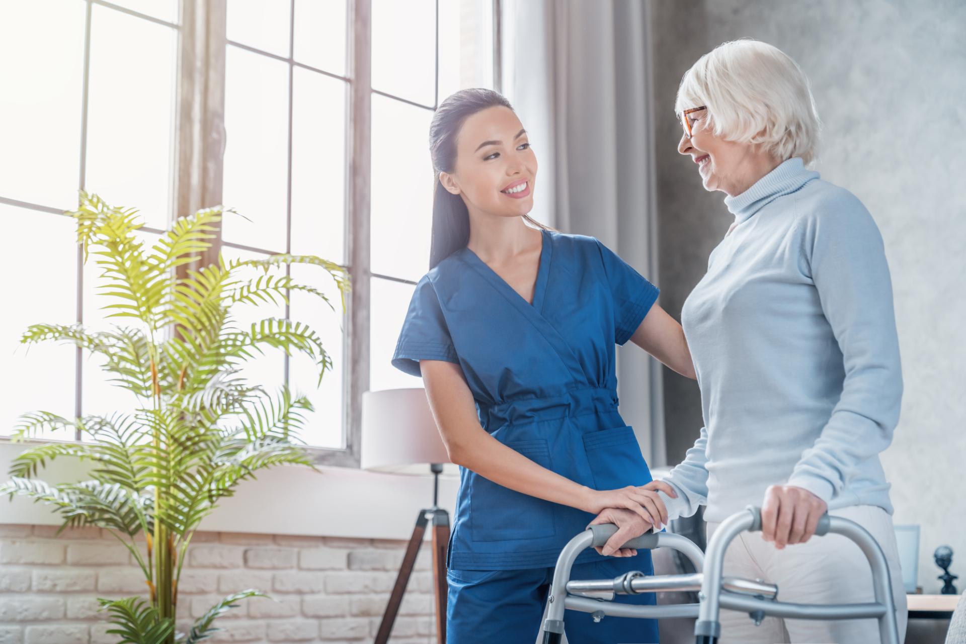 A carer supporting an older woman as she walks with a frame