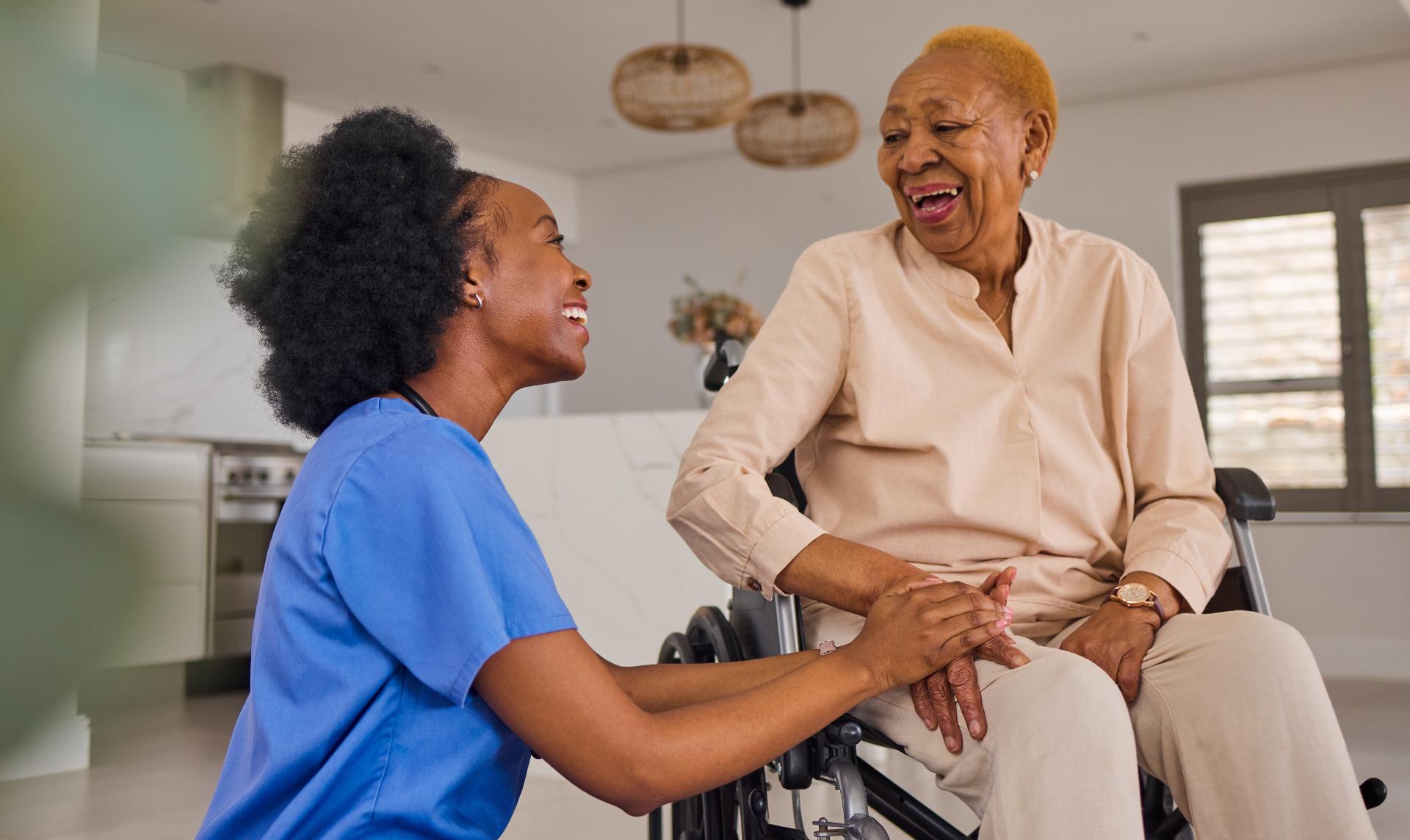 A carer and an older woman laughing together in her kitchen