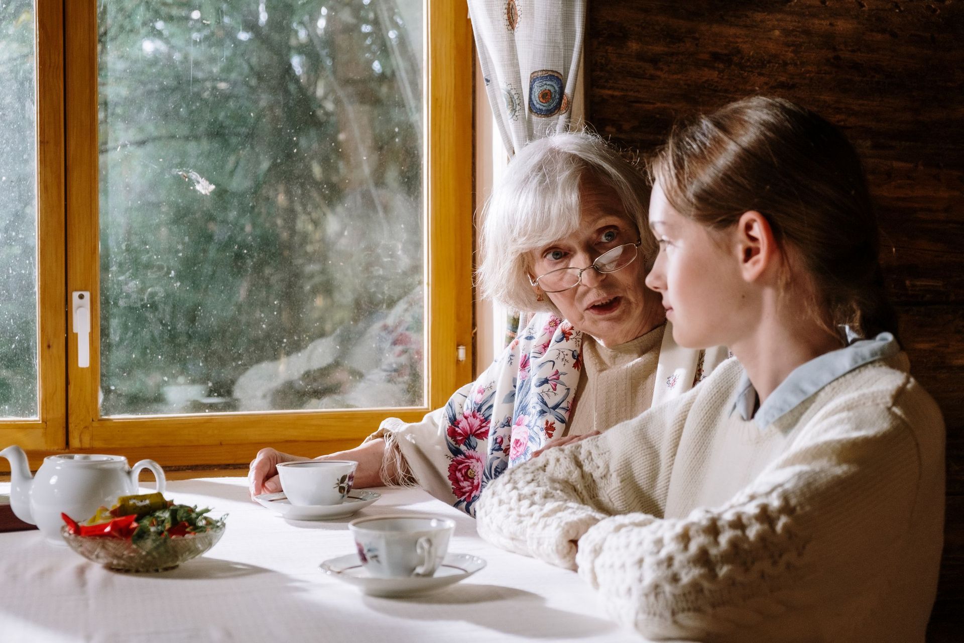 An older woman and a younger woman talking over tea by a window