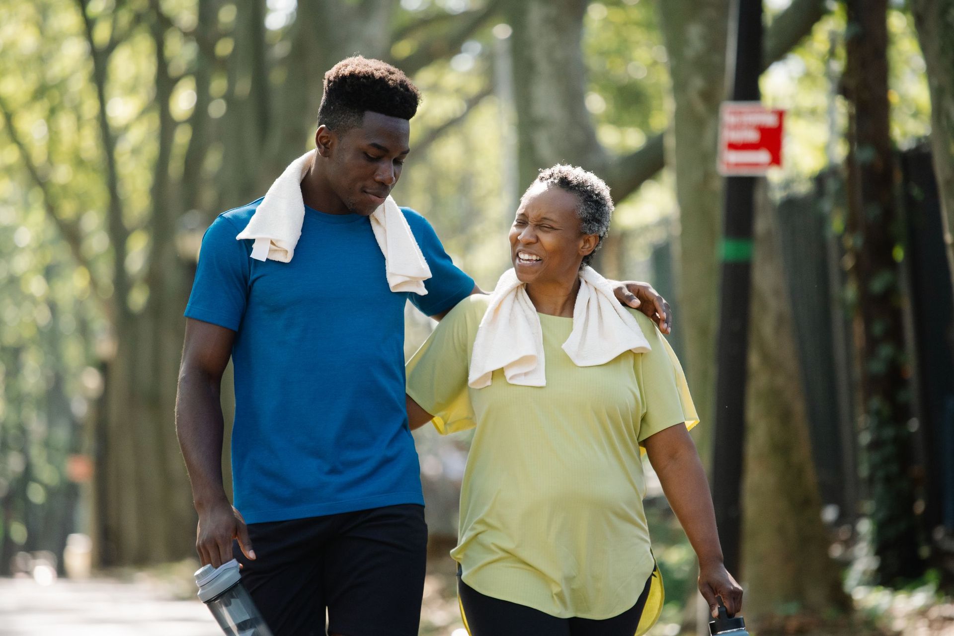 A young man and an older woman walking arm in arm along a tree-lined path