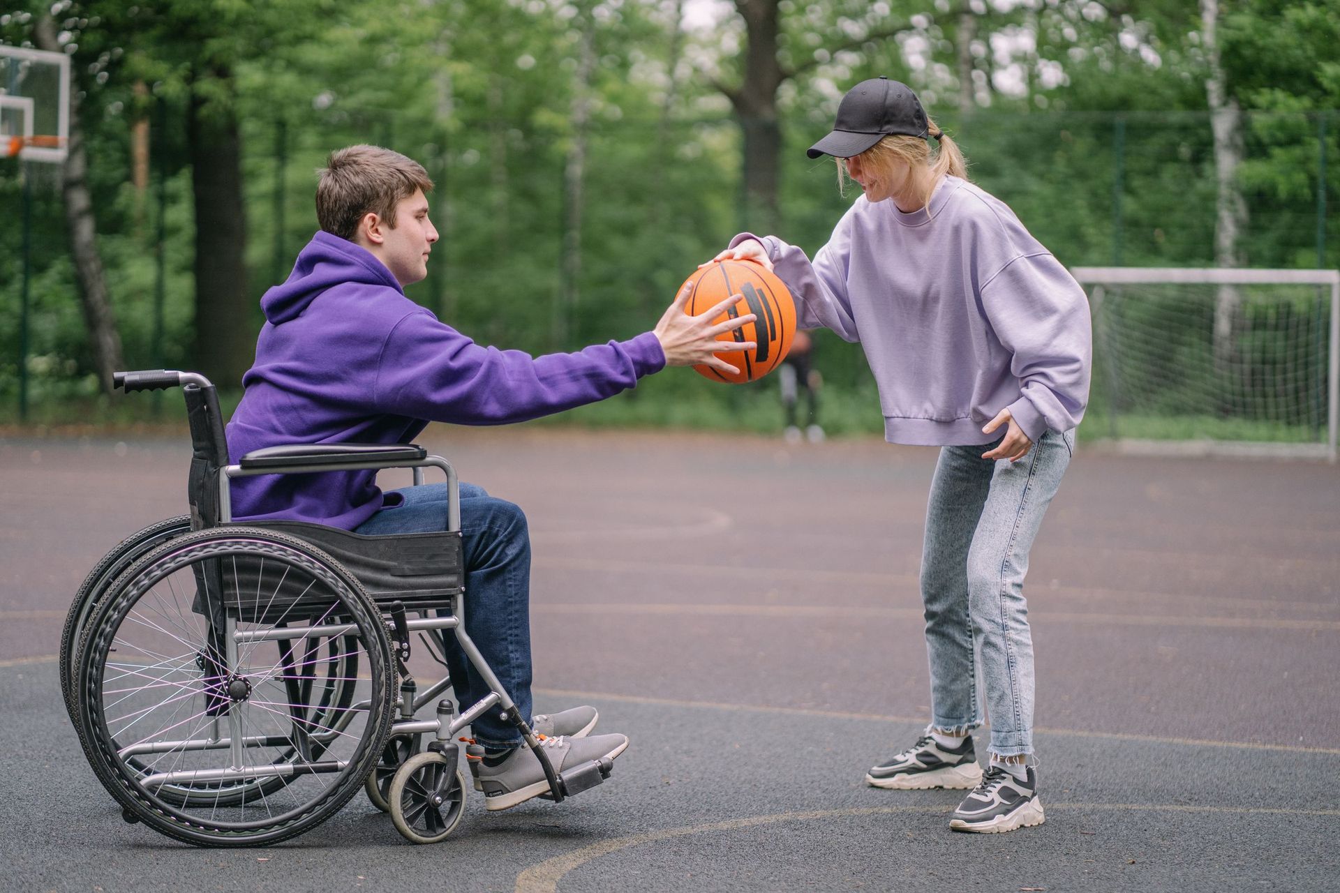 A young man in a wheelchair playing basketball with a friend in the park