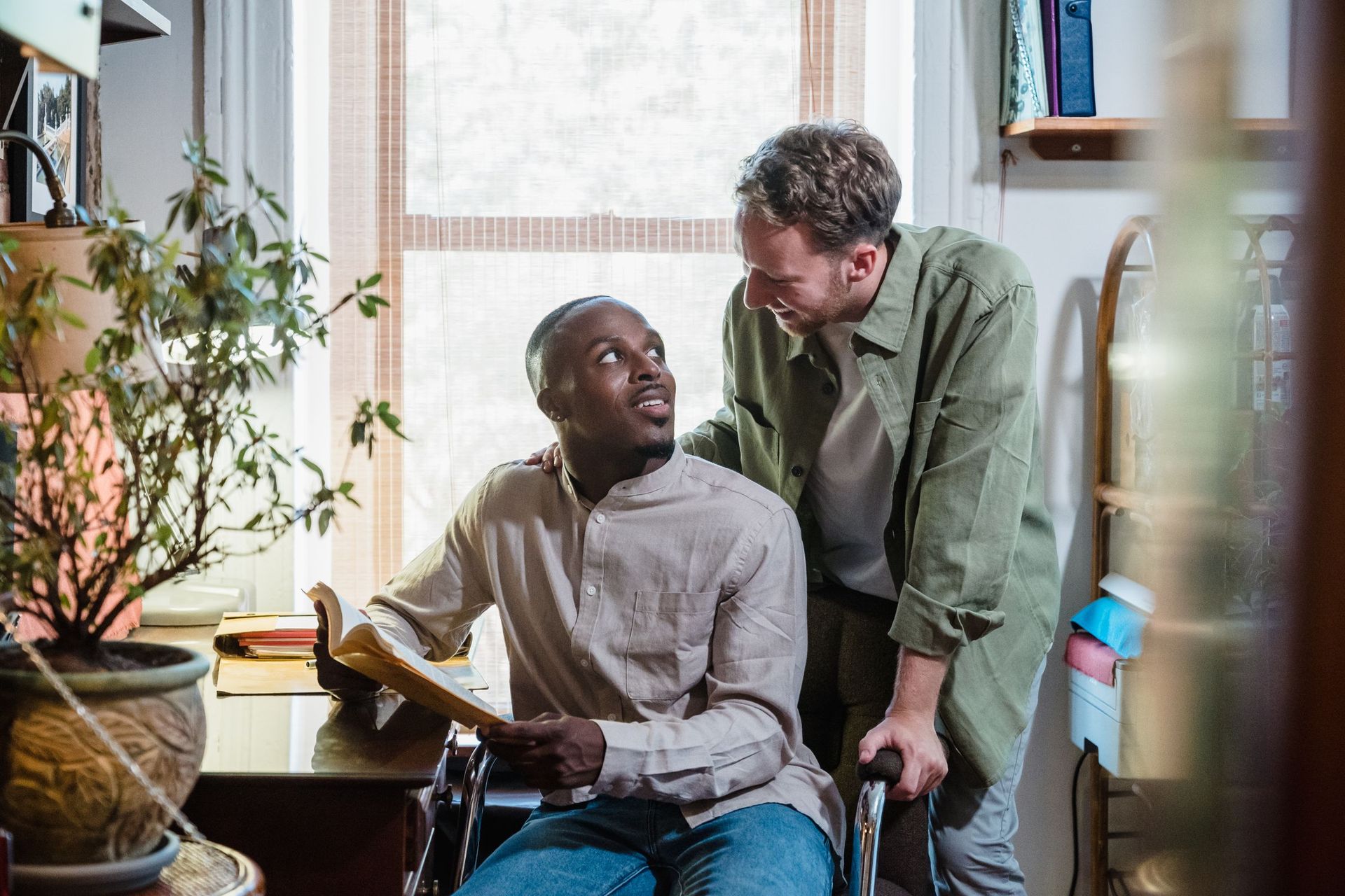 A man in a wheelchair smiling up at the man standing beside him at home