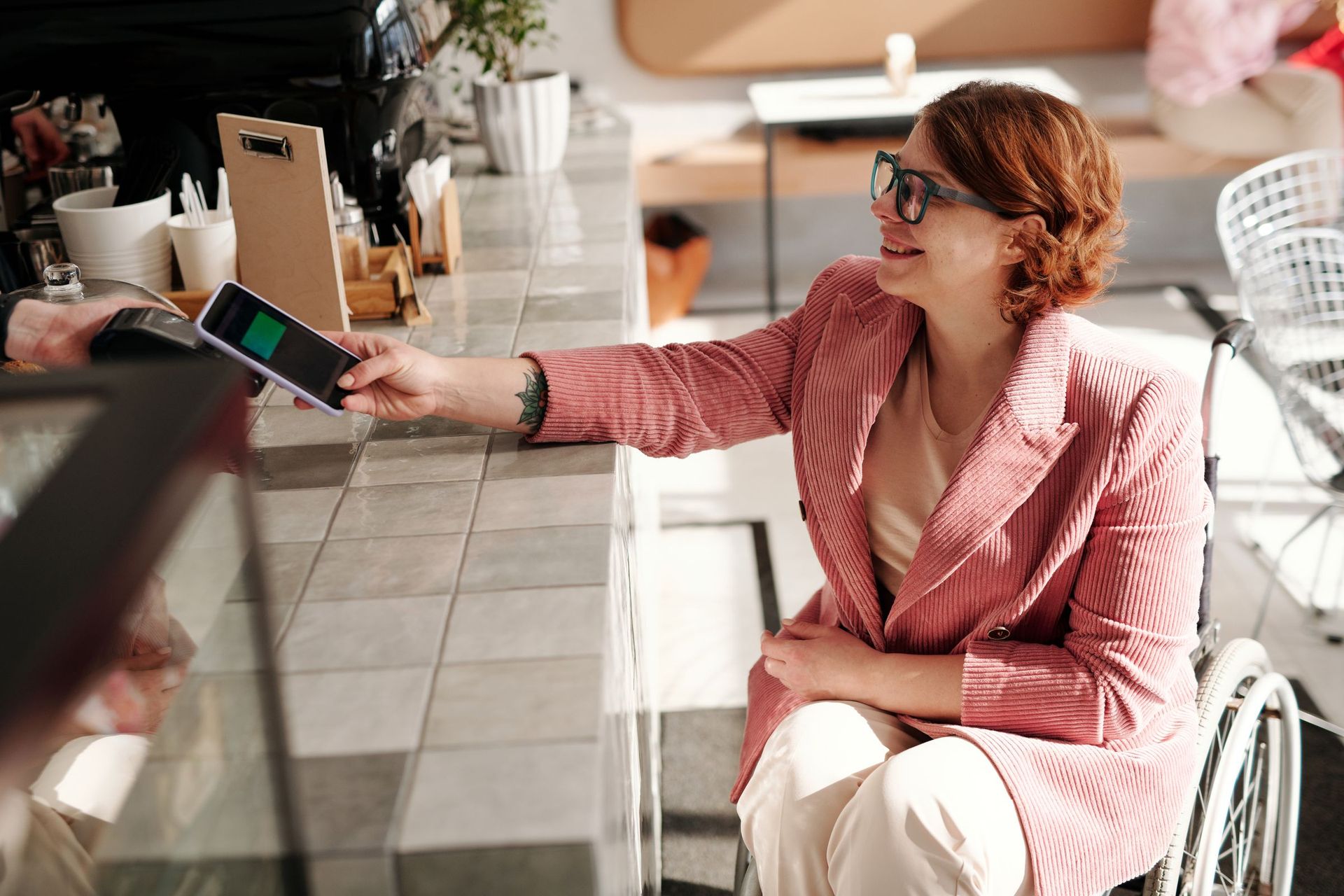 A woman in a wheelchair paying with her phone at a café counter
